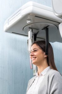 Close up side view portrait of woman taking dental examination with digital cone beam scanner machine in clinic.